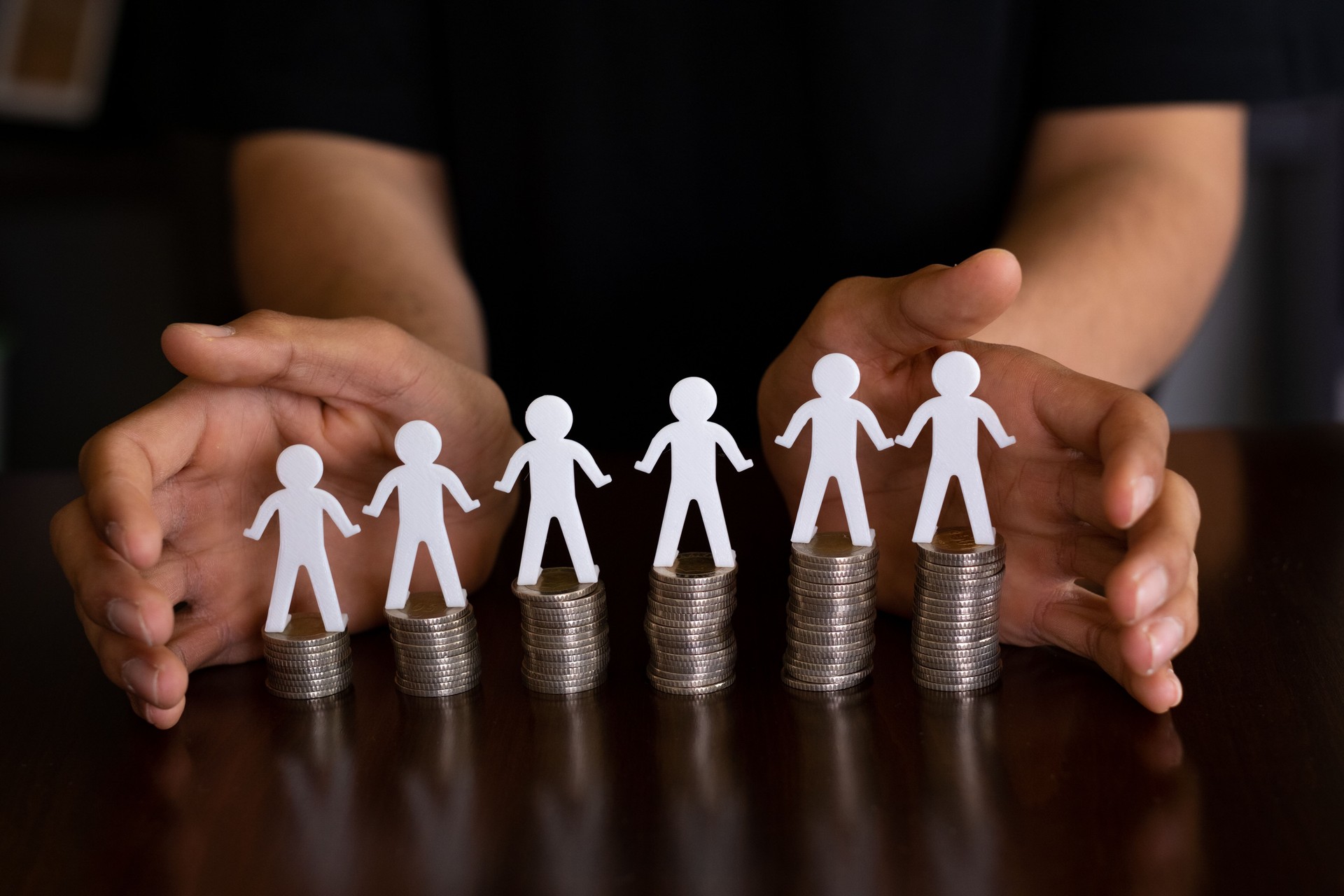 Man protecting human figures and coins holding hands